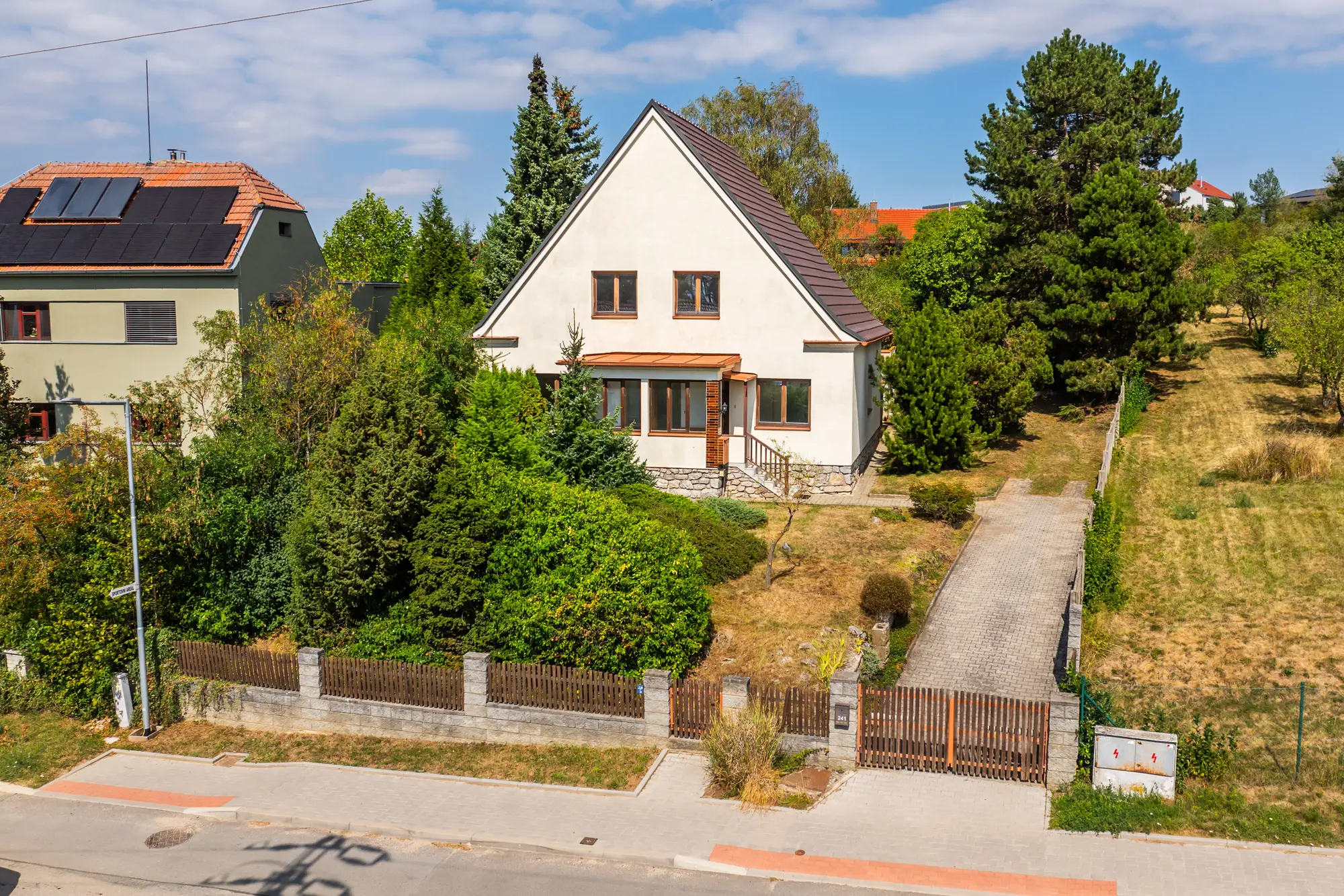 Pohled z dronu na dům od ulice, vjezd s bránou a chodník k domu