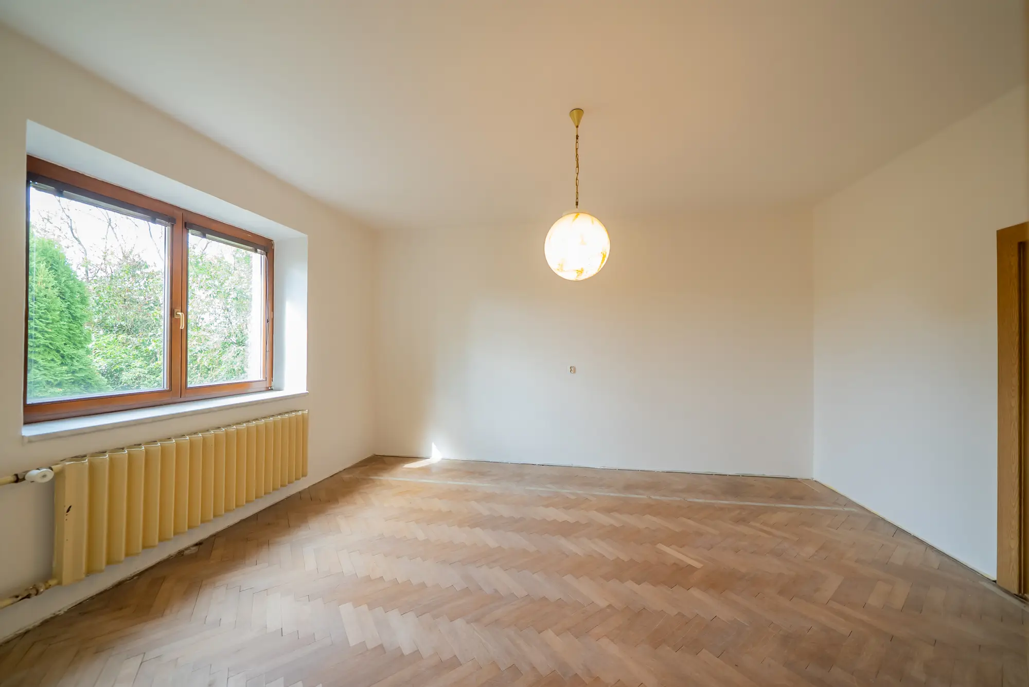 Pokoj v přízemí s parketovou podlahou a oknem do zahrady