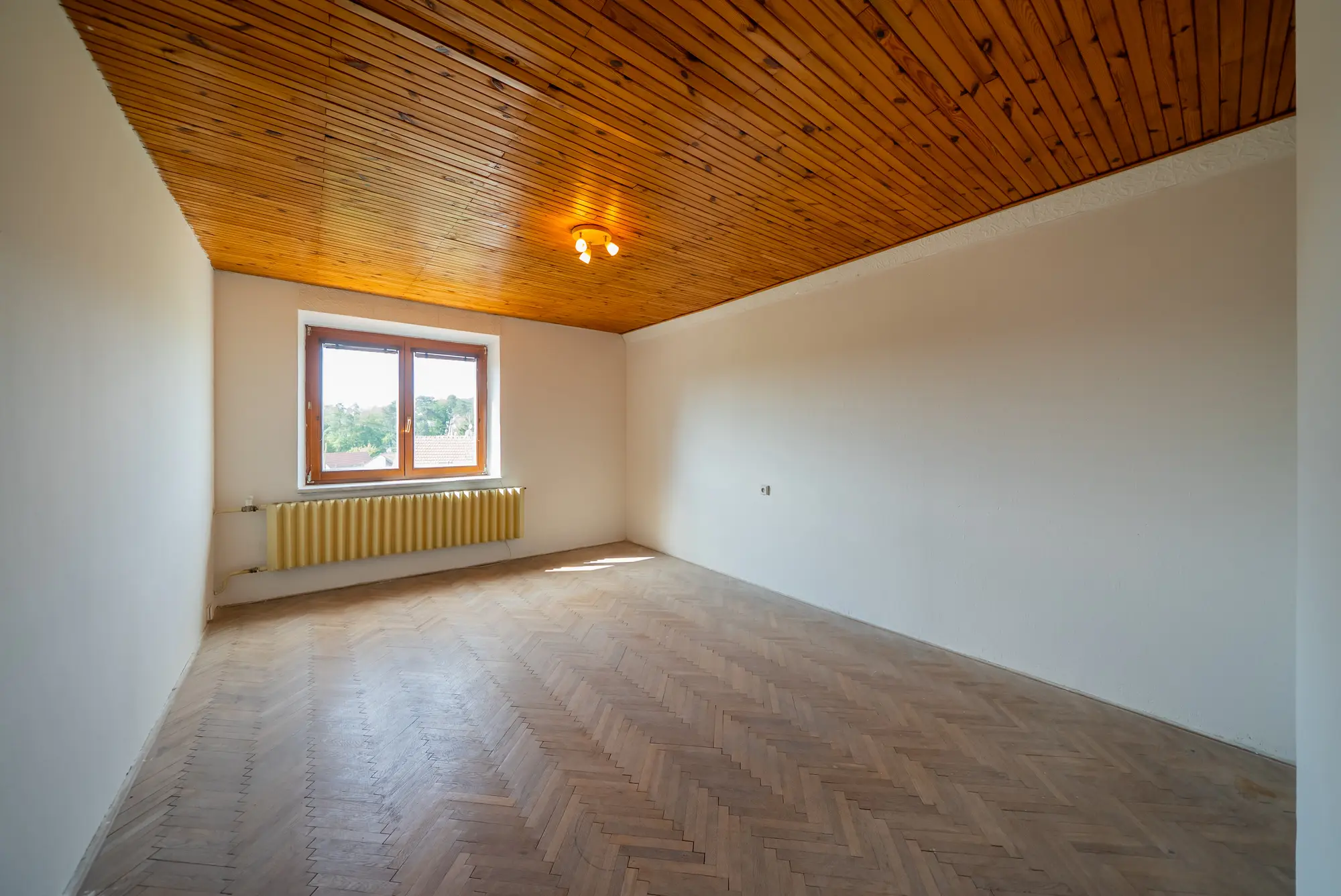 Pokoj v patře s dřevěným podhledem a šikmou stěnou
